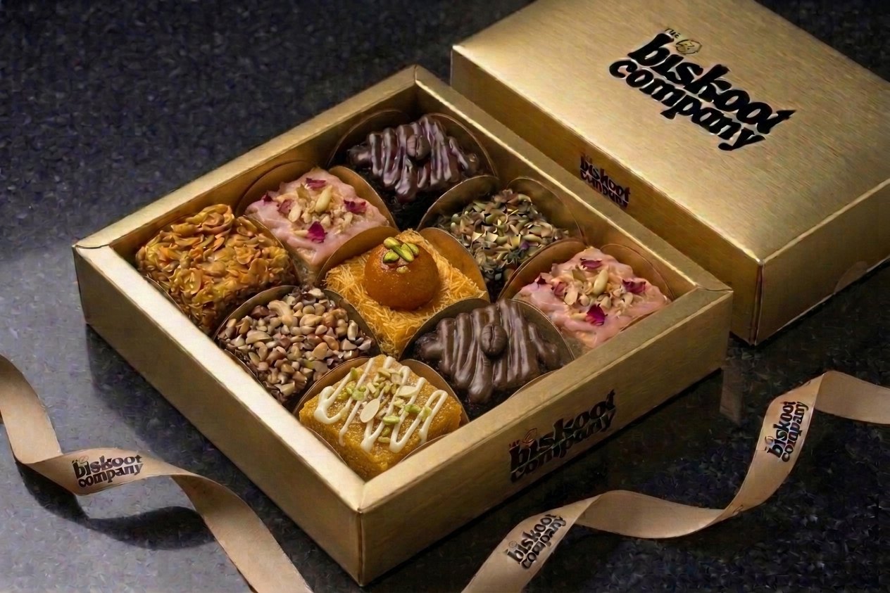 A gold Biskoot gift box holding brownies, blondies and a Gulab Jamun blondie, with the printed lid beside it